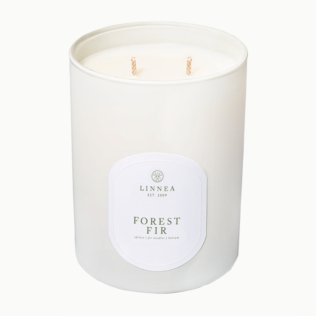 A white two-wick soy candle in a matte white glass jar with a white oval label reading LINNEA and FOREST FIR, photographed on a clean white background.
