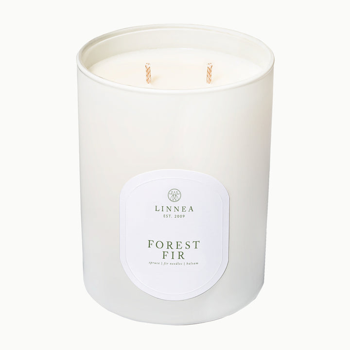A white two-wick soy candle in a matte white glass jar with a white oval label reading LINNEA and FOREST FIR, photographed on a clean white background.