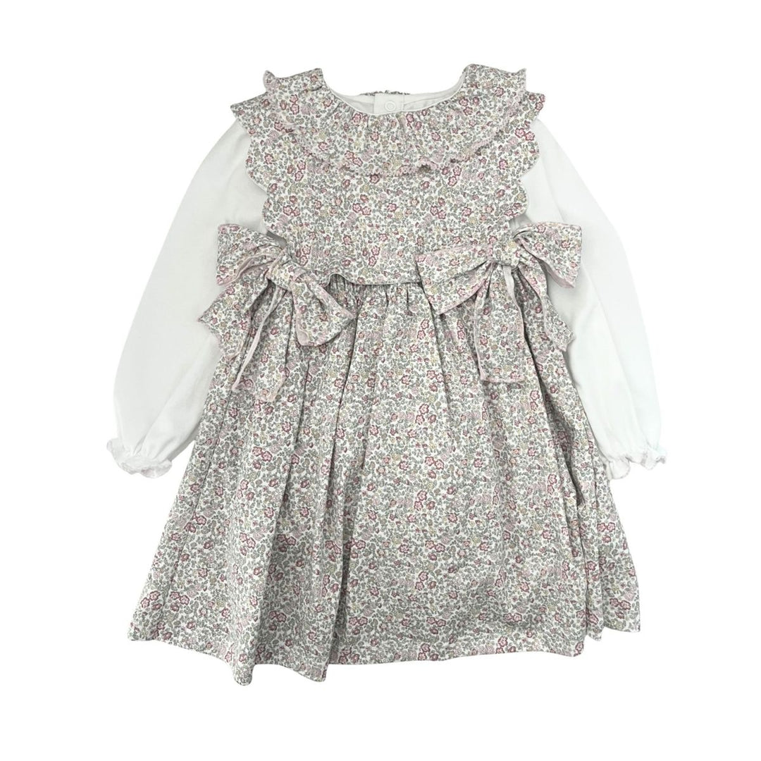 A toddler girl's long-sleeve dress featuring a white long-sleeve base and a ruffled, tiered bodice with a dense small floral print in muted pink, green, and gray tones. The dress has a ruffled collar, a gathered waist with two bows, and a flared skirt.