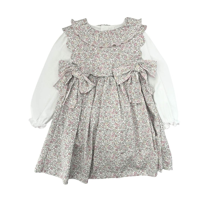 A toddler girl's long-sleeve dress featuring a white long-sleeve base and a ruffled, tiered bodice with a dense small floral print in muted pink, green, and gray tones. The dress has a ruffled collar, a gathered waist with two bows, and a flared skirt.