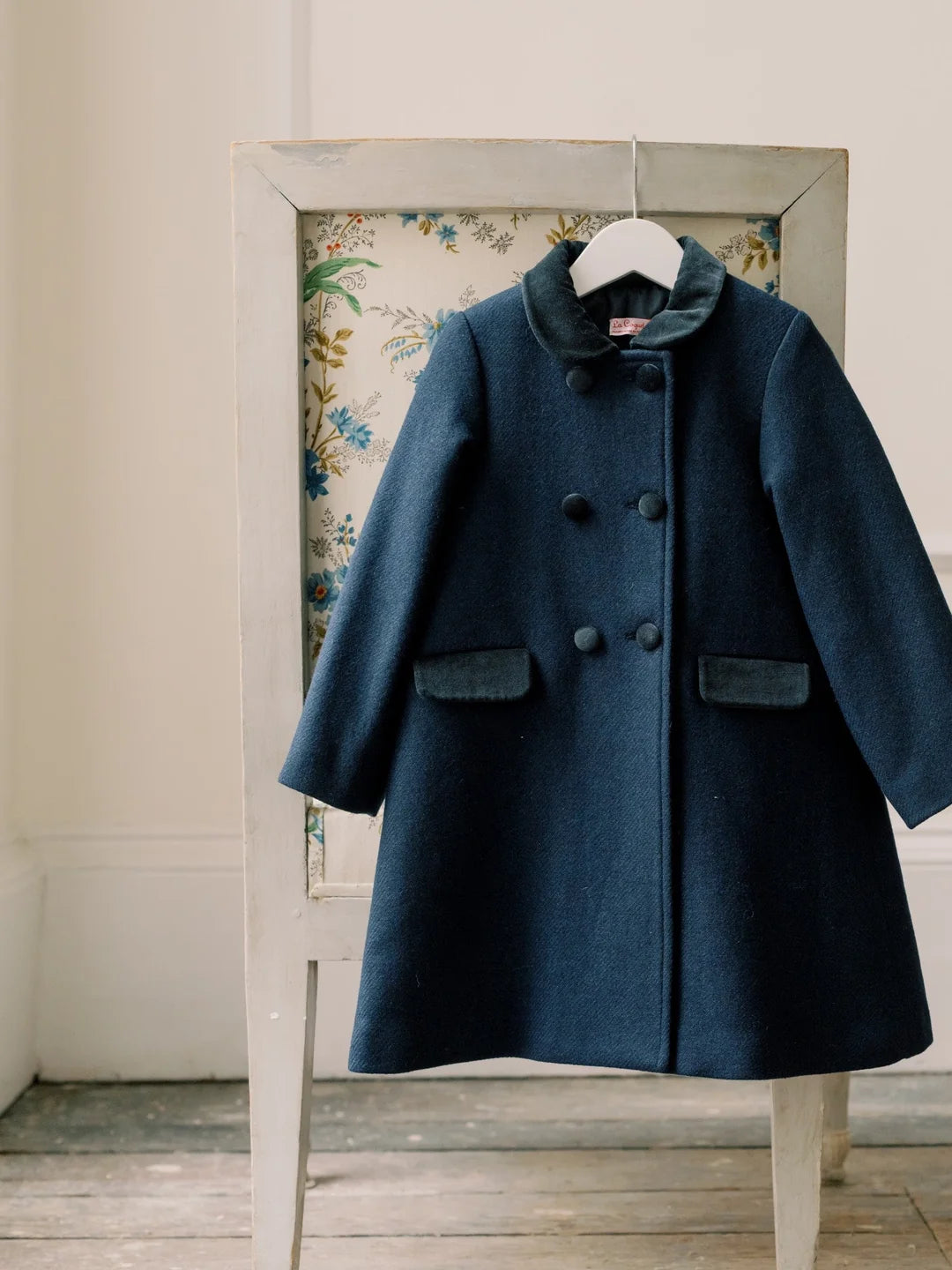 Blue coat hanging on a rack against a floral-patterned wall.