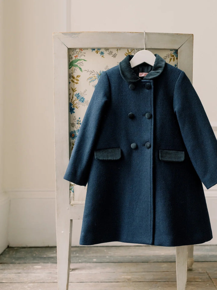 Blue coat hanging on a rack against a floral-patterned wall.