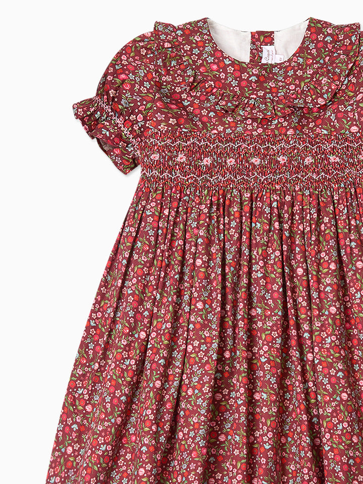 A close-up of a short-sleeve dress with a red, pink, and white floral print, featuring a smocked bodice and ruffled neckline.