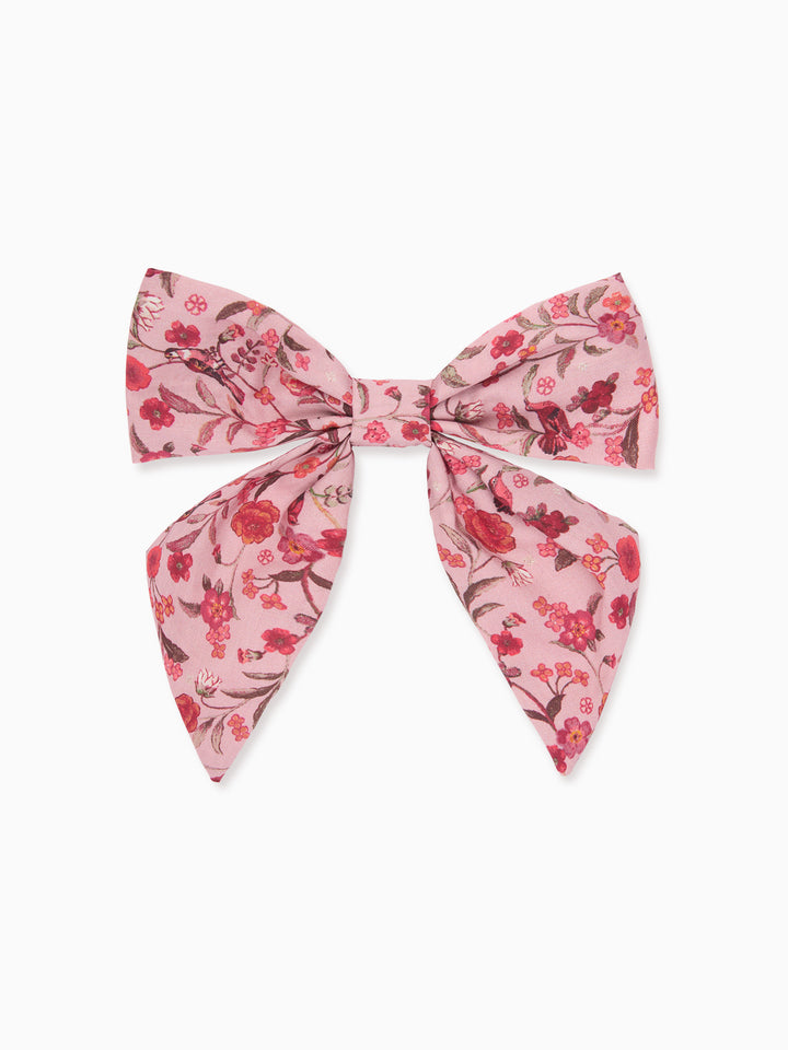A pink bow accessory with a red and green floral pattern, displayed flat against a light gray background.