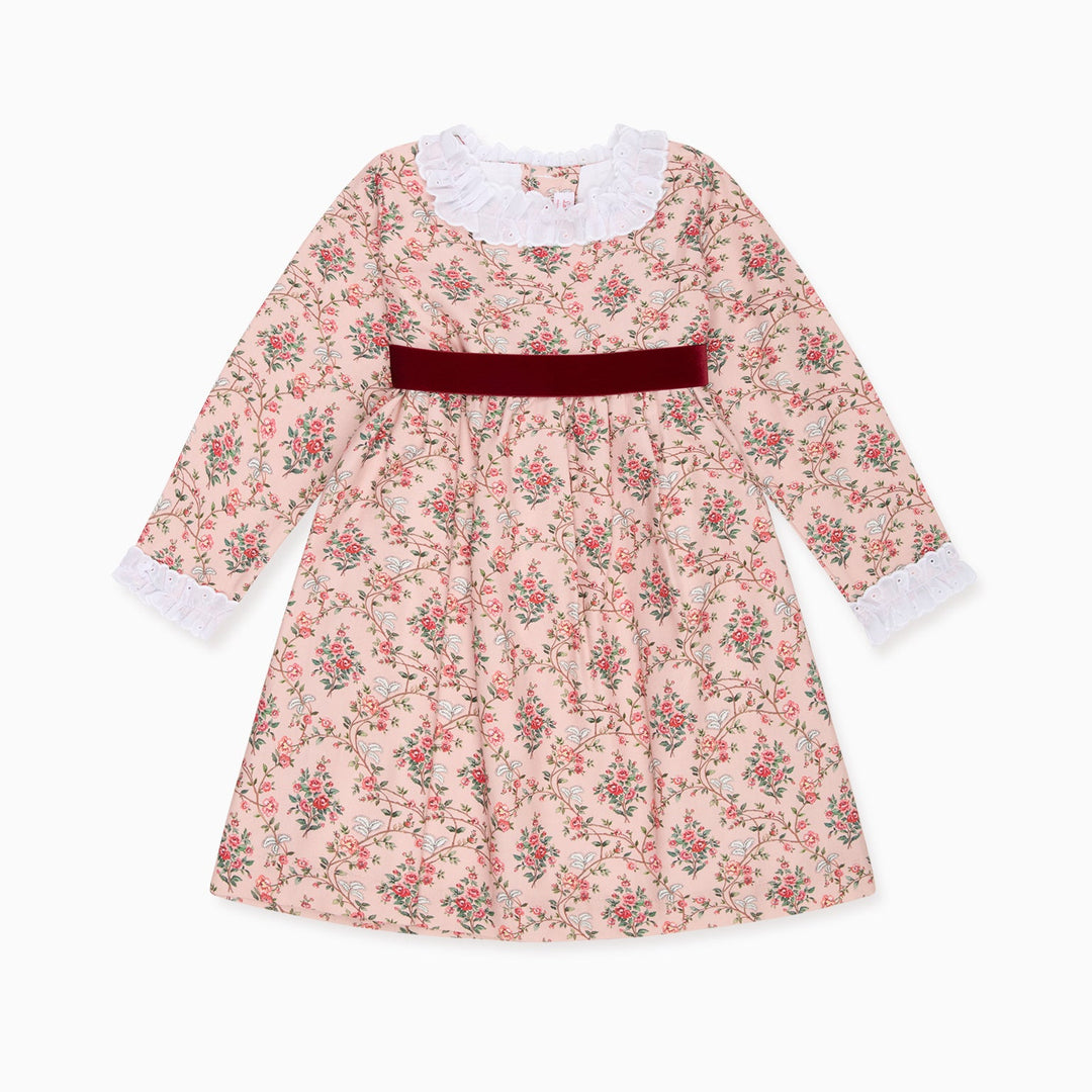 A long-sleeve girl's dress with a pink and green floral print, featuring a white ruffled collar, white ruffled cuffs, and a dark red velvet waist sash, shown against a plain white background.