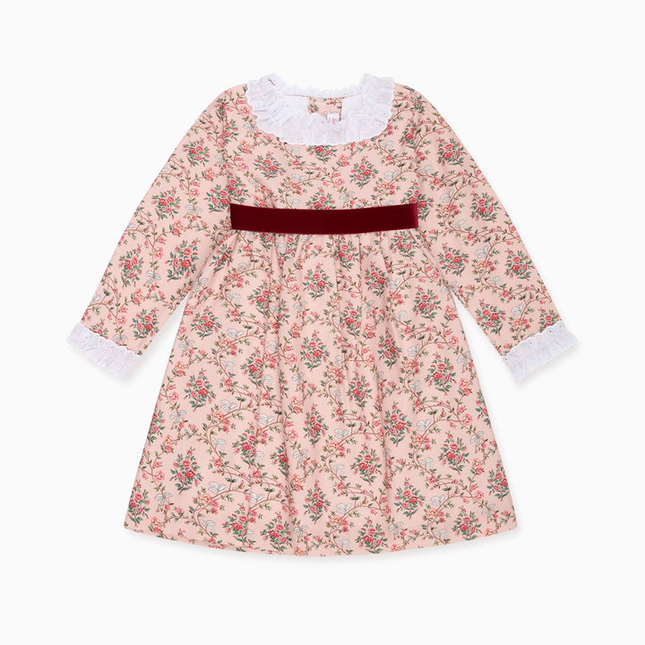 A long-sleeve girl's dress with a pink and green floral print, featuring a white ruffled collar, white ruffled cuffs, and a dark red velvet waist sash, shown against a plain white background.