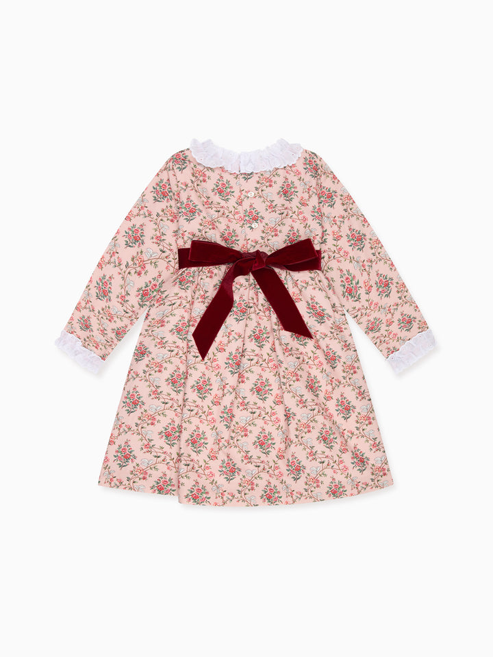 A long-sleeve baby dress with a pink and red floral print, featuring a dark red velvet bow at the waist and white ruffled trim at the collar and cuffs, shown on a plain white background.
