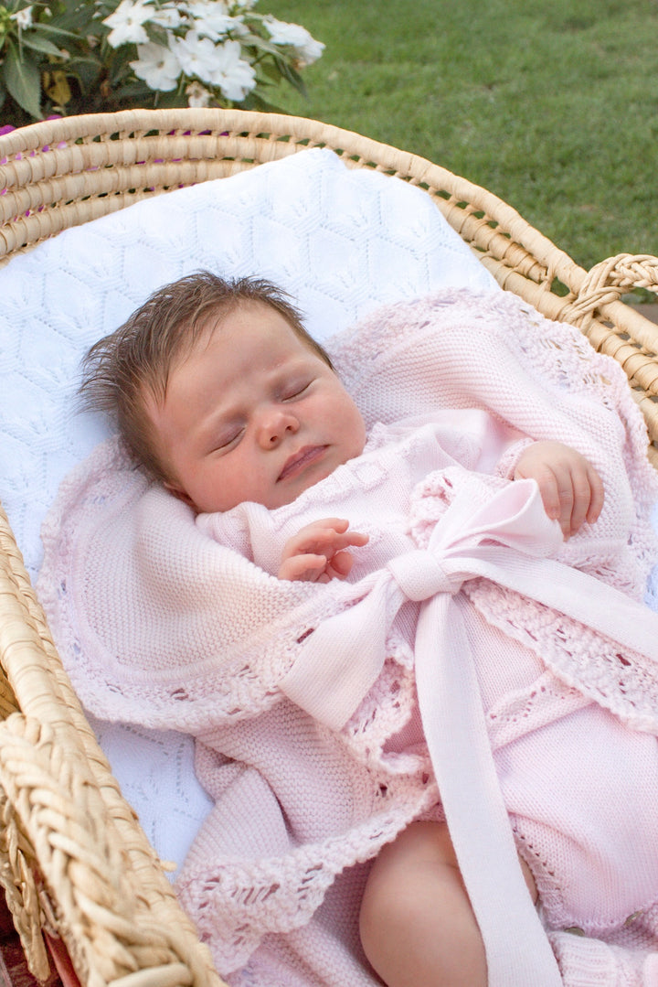 Newborn baby in a pink outfit lying in a wicker basket with a white blanket.