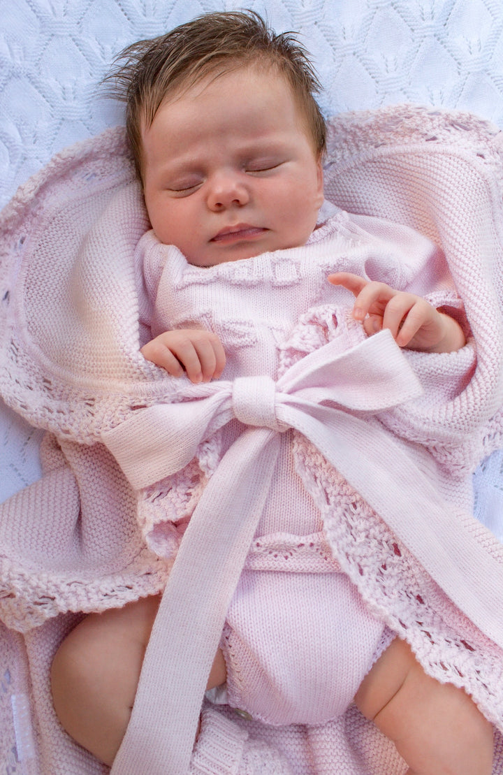 Newborn baby wrapped in a pink blanket with a bow, lying on a textured surface.