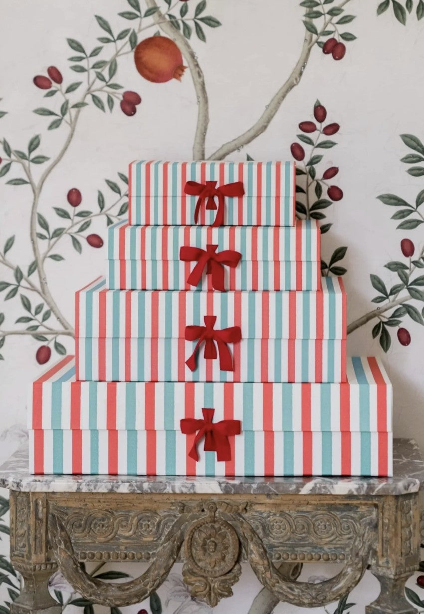 A stack of La Coqueta Gift Boxes sitting on a decorative side table against a pomegranate wallpaper