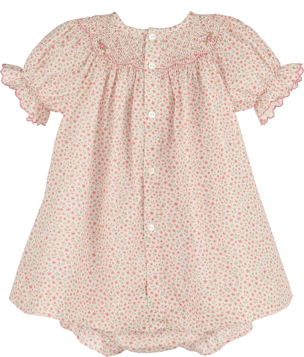 A baby girl's smocked dress with short flutter sleeves, featuring a delicate pink and green floral print on a cream background, with white buttons down the front.