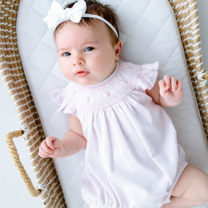 Baby in a white outfit with a bow headband lying on a white cushion.