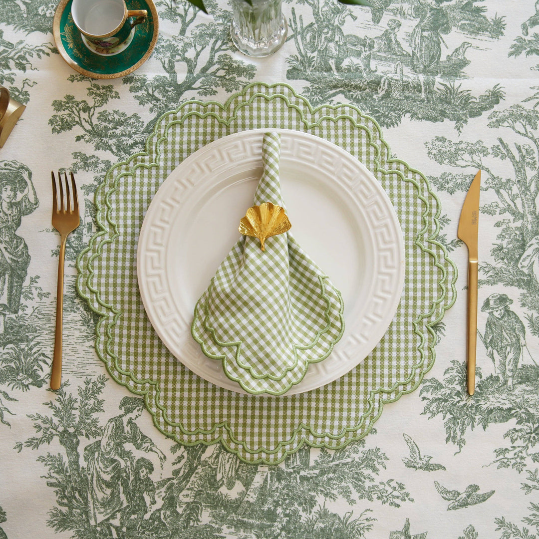Table setting with green checkered napkin, white plate, and cutlery on a patterned tablecloth.