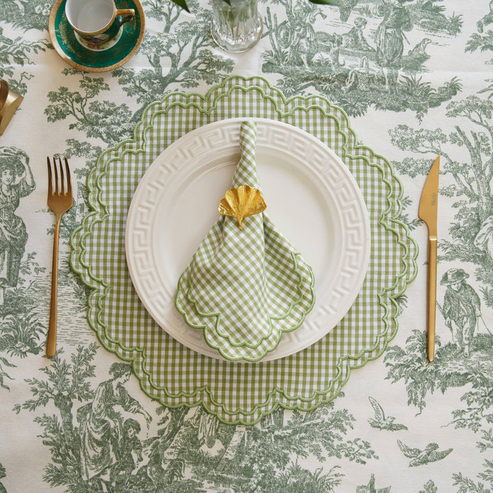Table setting with green checkered napkin, white plate, and cutlery on a patterned tablecloth.