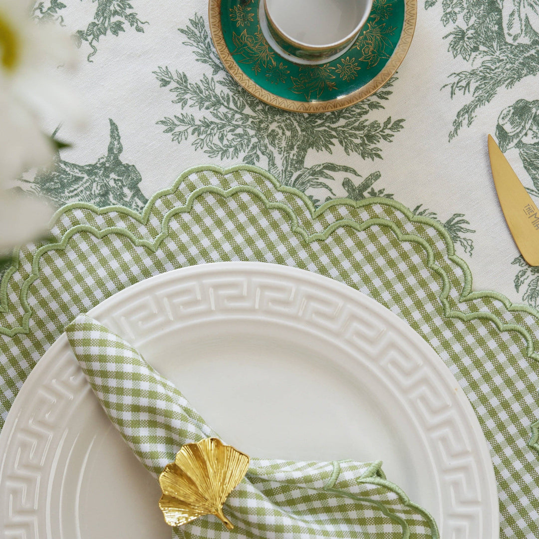 Table setting with green checkered napkin, white plate, and gold napkin ring on a patterned tablecloth.