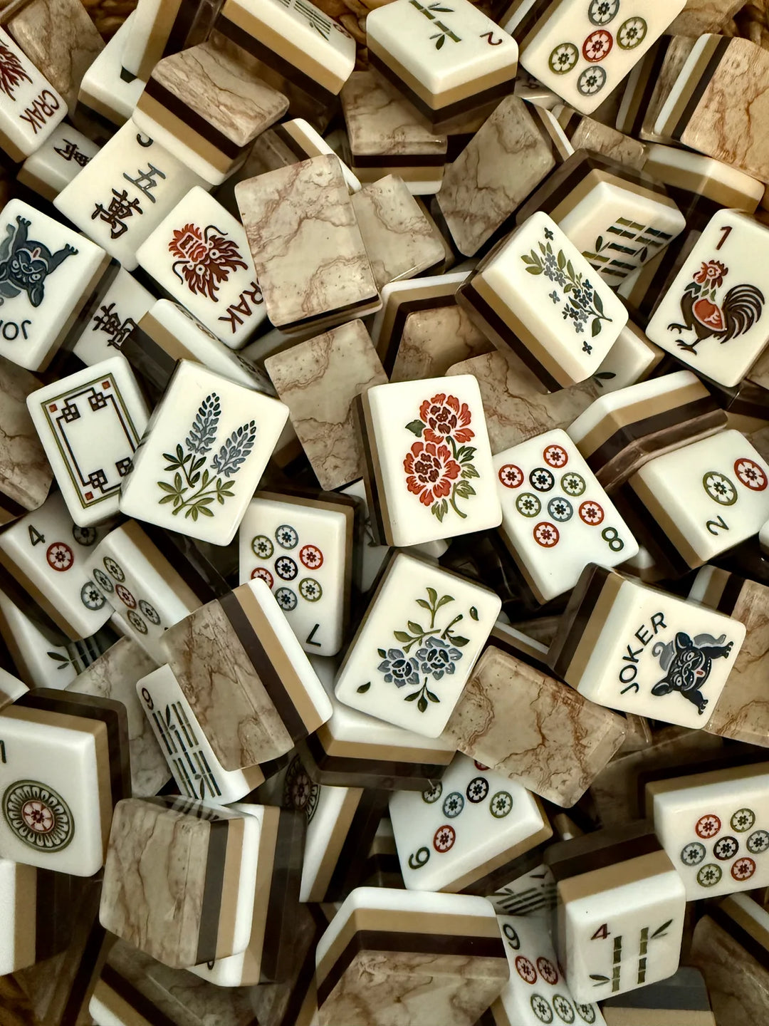 A dense pile of Mahjong tiles with cream-colored backs, brown marble-look borders, and various colorful floral and symbol faces.