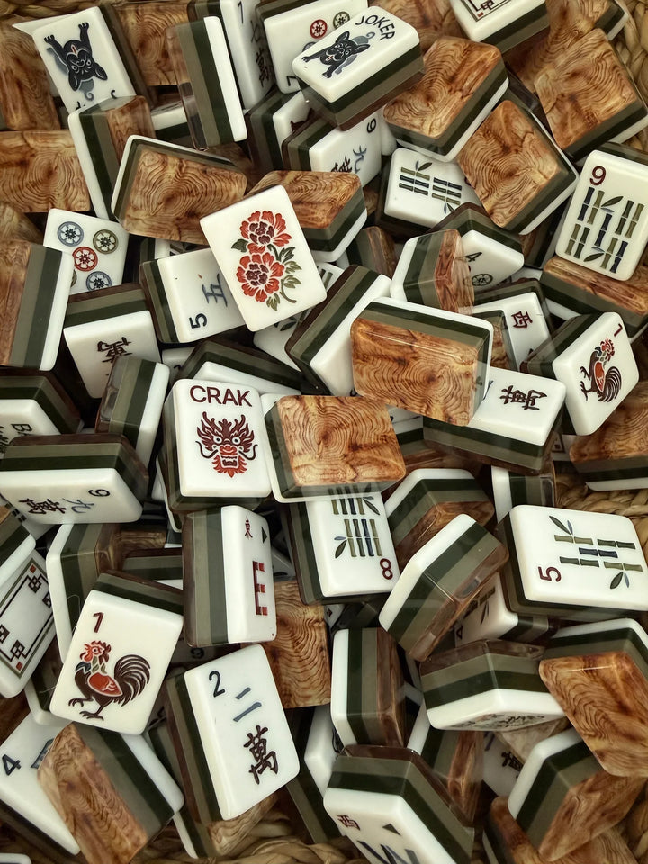 A pile of Mahjong tiles with white faces showing black Chinese characters and colorful floral or animal motifs, alongside wood-grain-patterned backs.
