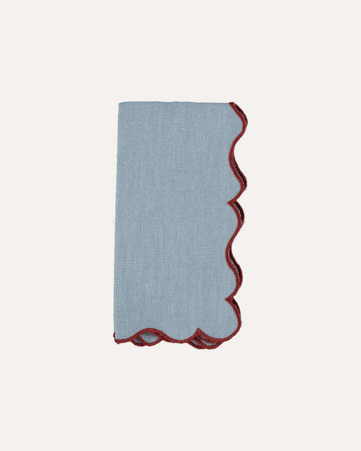 A folded light blue linen pocket square with a scalloped edge trimmed in dark red, shown on a plain off-white background.