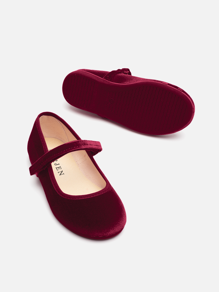 A pair of burgundy velvet Mary Jane shoes, with one shoe showing the side and strap and the other showing the sole, on a light gray background.