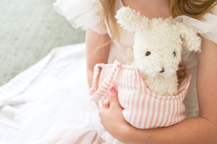 Child holding a white puppy in a pink striped bag