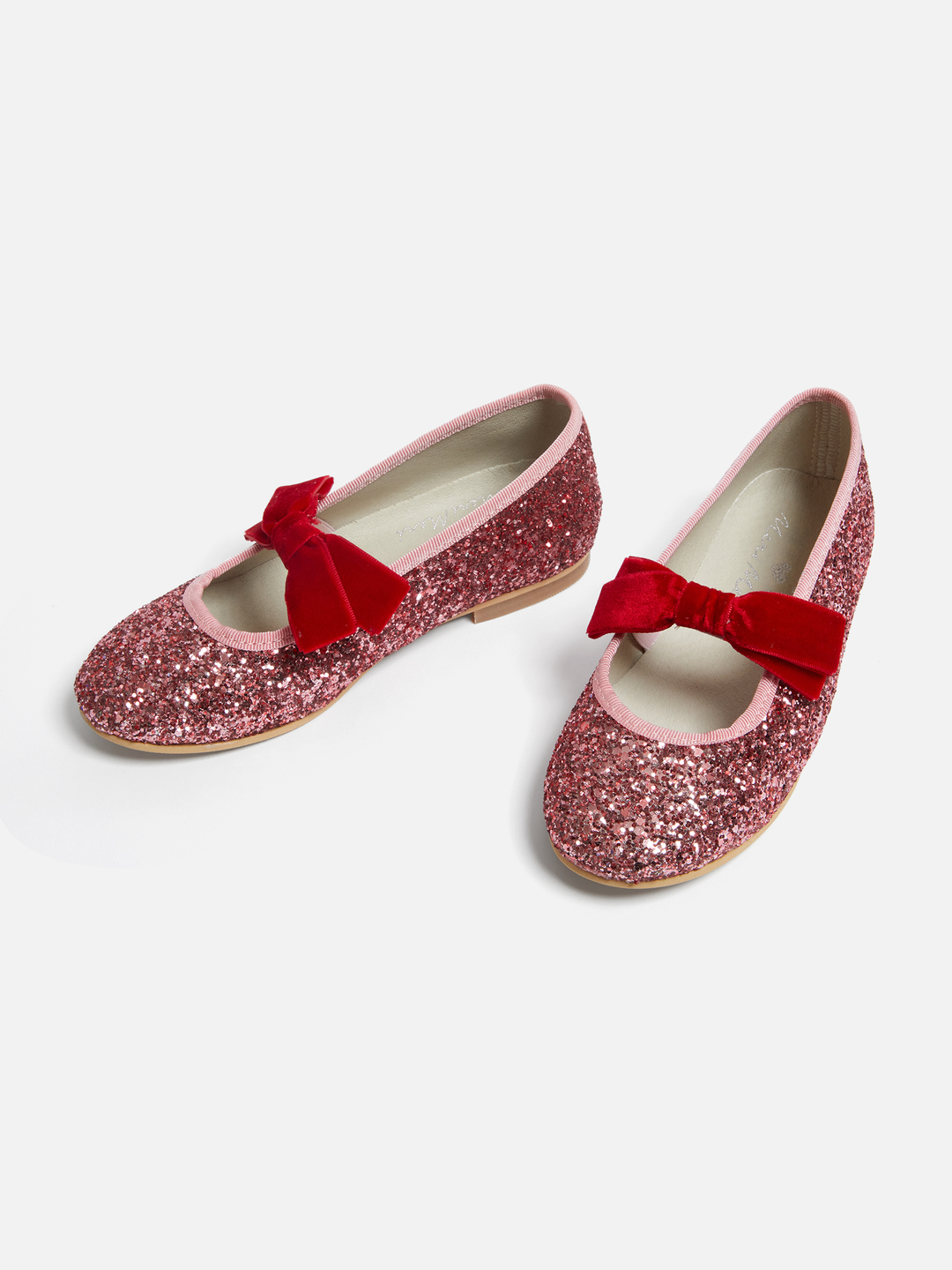 A pair of sparkly pink glitter Mary Jane shoes with red velvet bow details, displayed on a clean light gray background.