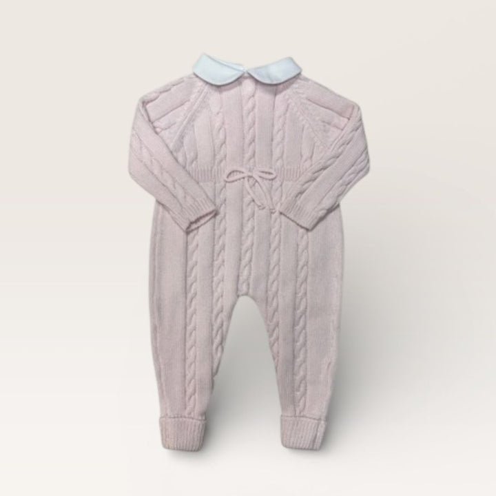 A baby cable-knit jumpsuit in a dusty lavender-pink color, featuring a light blue Peter Pan collar and a matching bow at the chest, displayed on a neutral cream background.