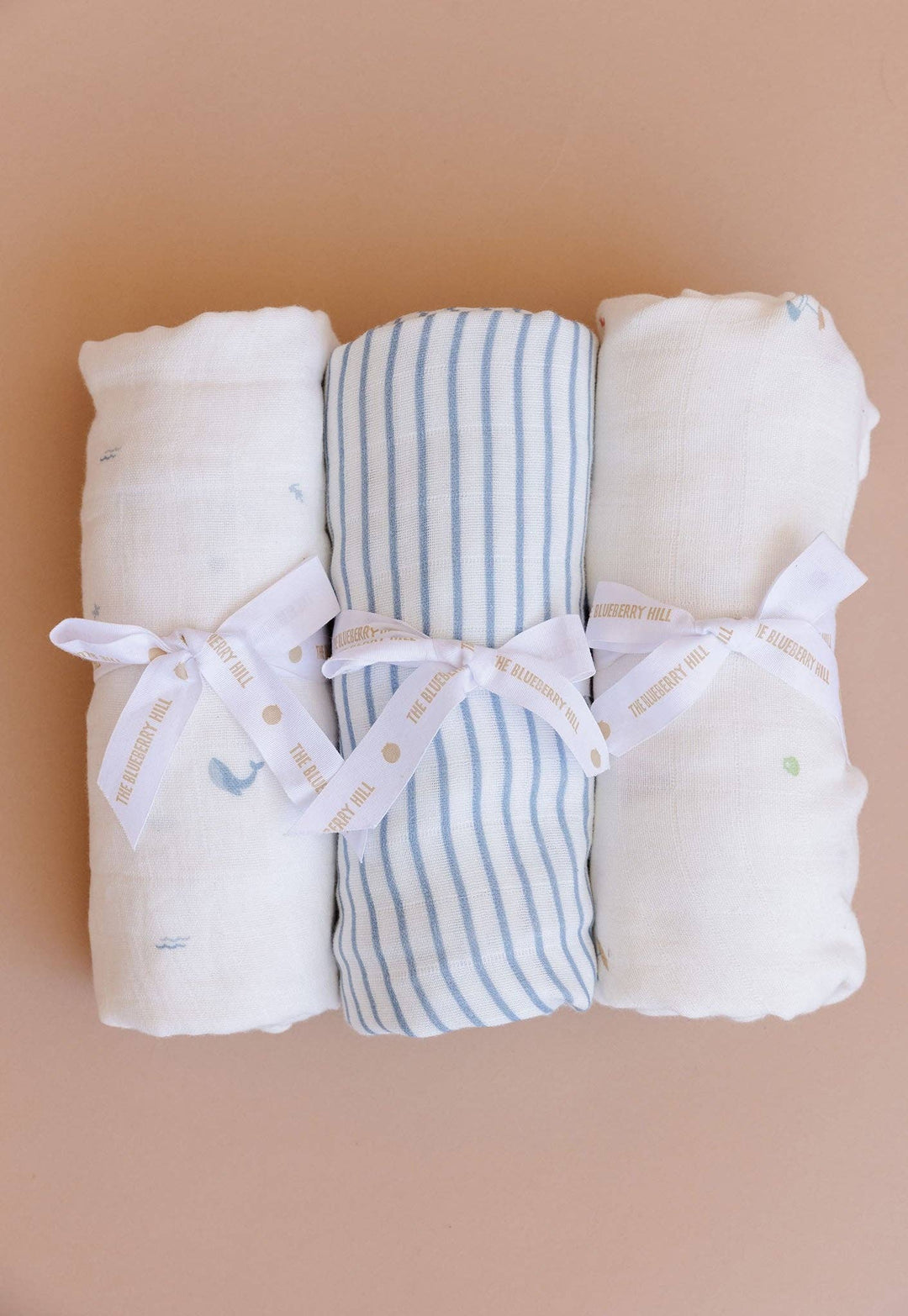 Three folded baby blankets with ribbons on a beige background