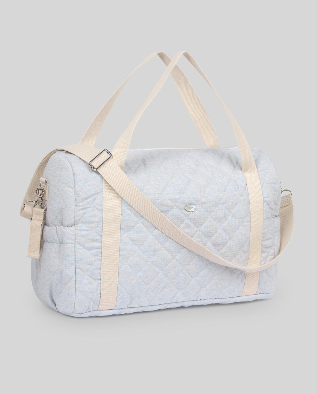 A light blue quilted duffel bag with beige handles and a matching shoulder strap, shown against a solid gray background.