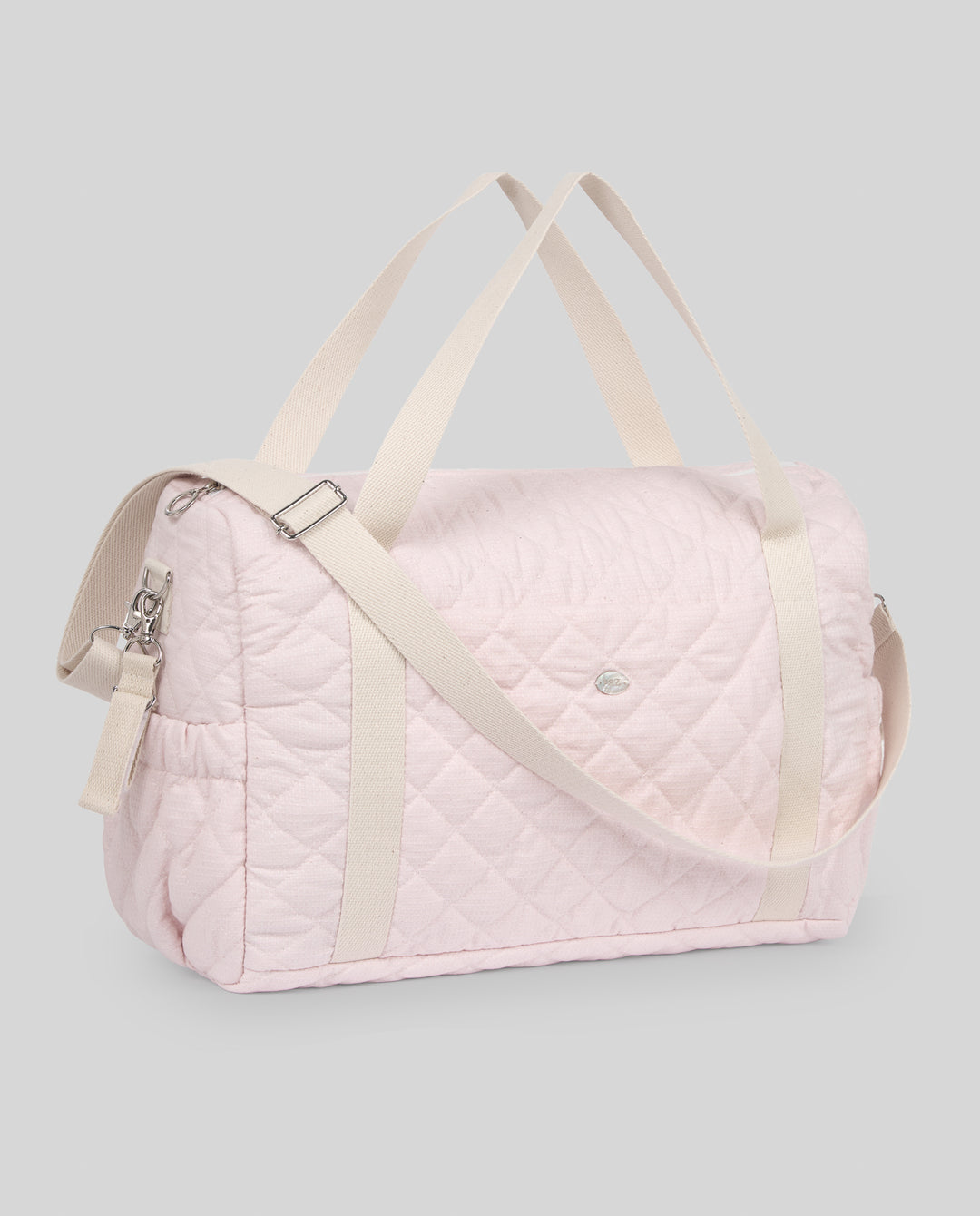 A light pink quilted duffel bag with cream-colored shoulder straps and side straps, shown on a solid gray background.