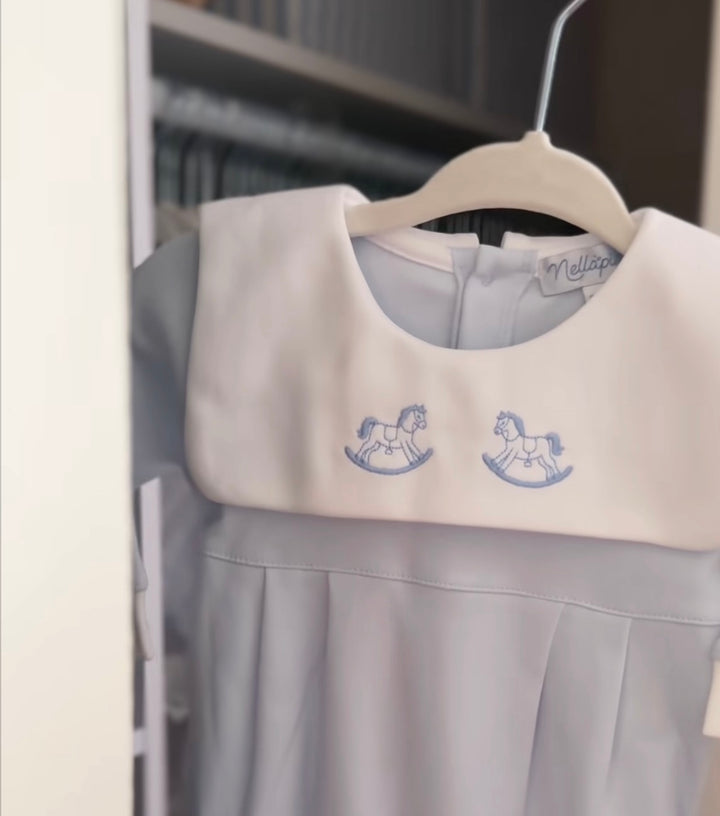 A close-up of a baby wearing a light blue onesie with a white cuff featuring a blue rocking horse logo, shown in a social media ad format.