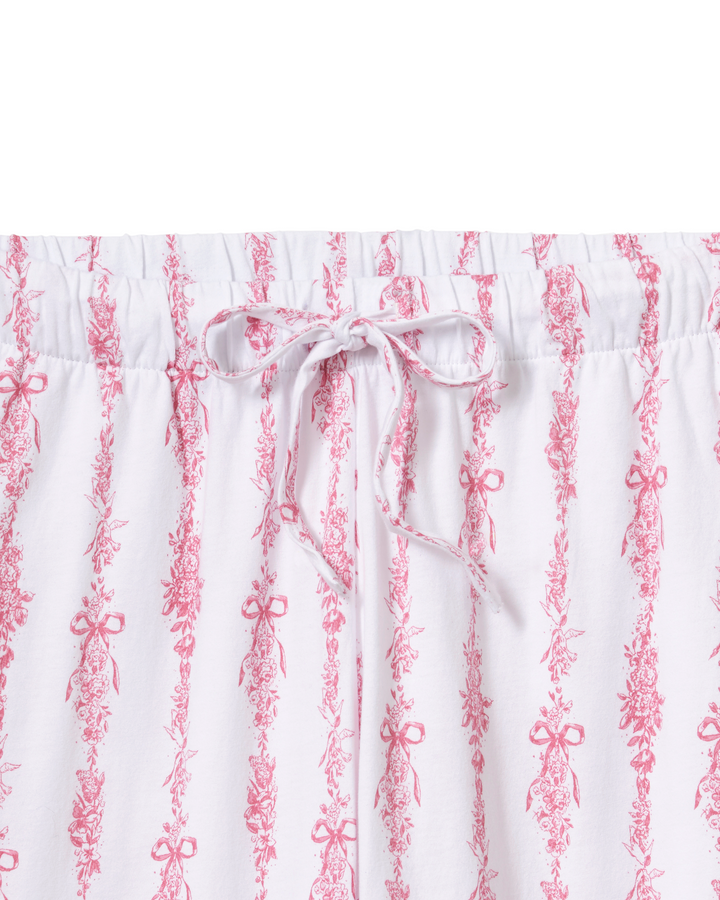 White drawstring shorts featuring a vertical pink toile-style pattern of bows and floral motifs, shown against a plain white background.