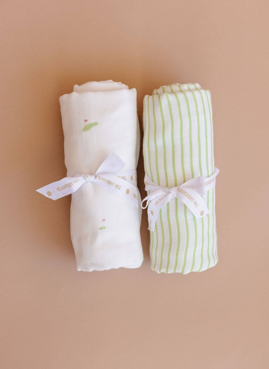Two rolled-up baby blankets with ribbons on a beige background