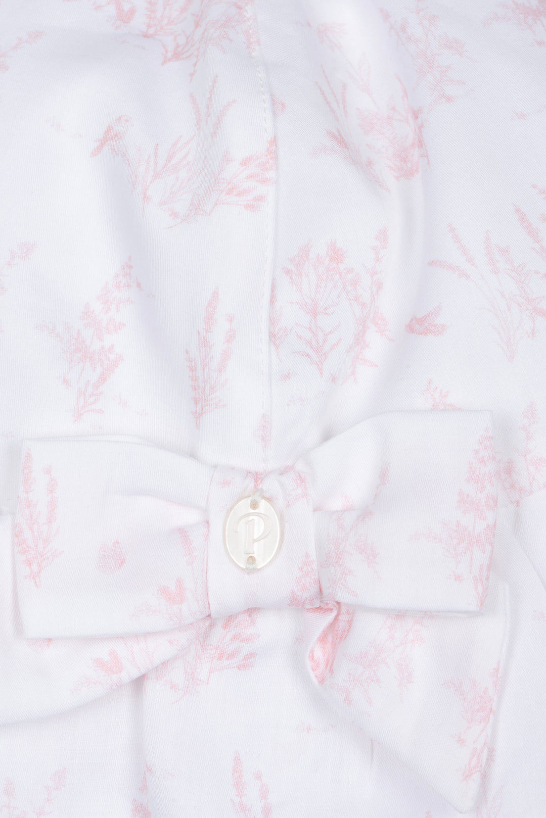 Close-up of a white shirt with pink floral pattern and a button on a white background