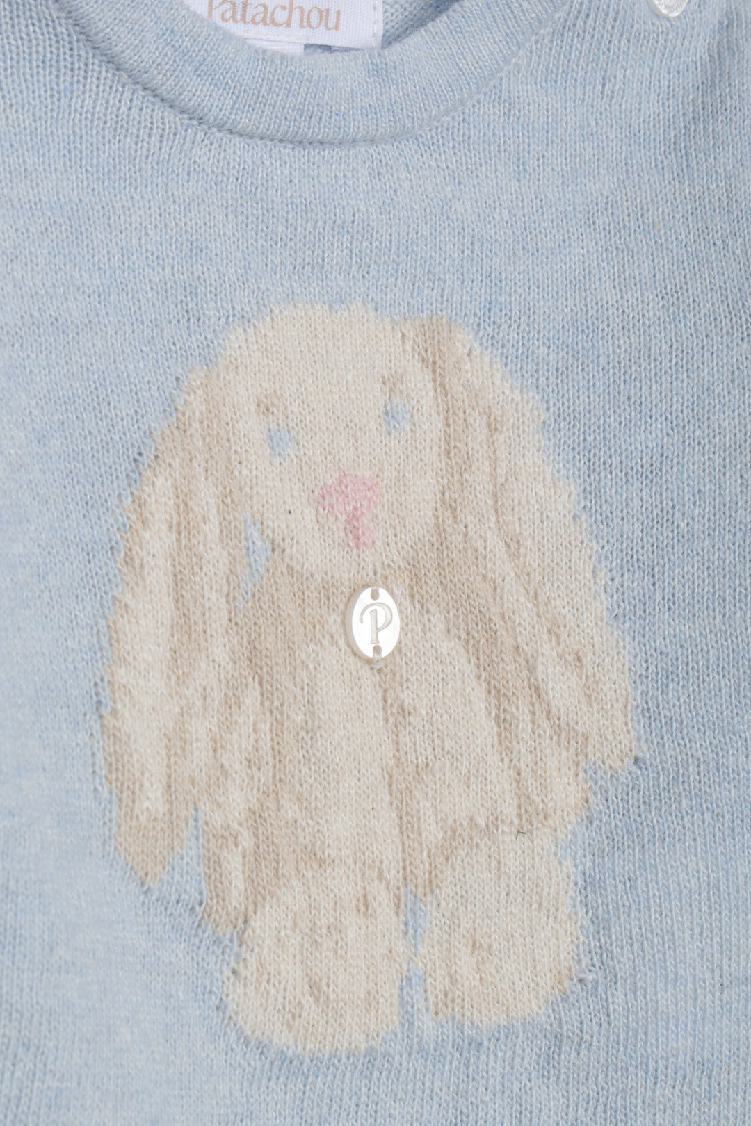 Close-up of a light blue knit sweater featuring a large cream-colored bunny motif with a pink nose and a silver button at the center.