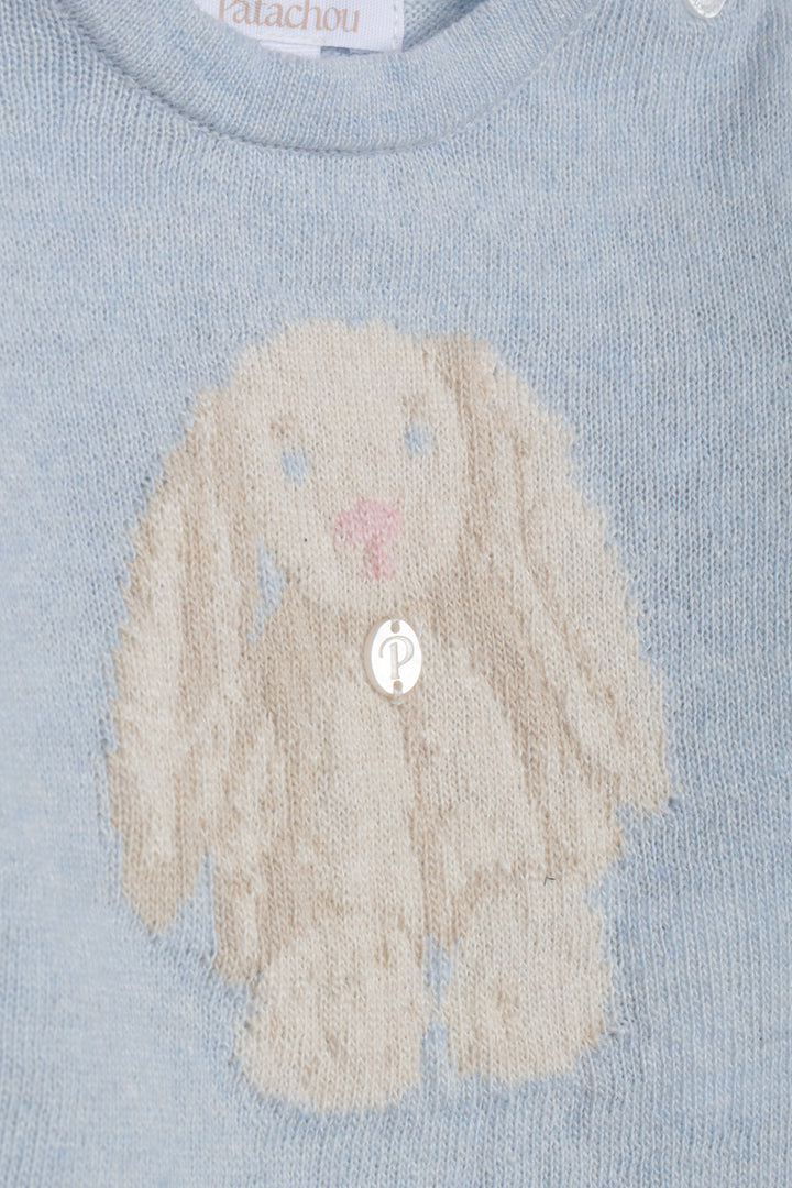 Close-up of a light blue knit sweater featuring a large cream-colored bunny motif with a pink nose and a silver button at the center.