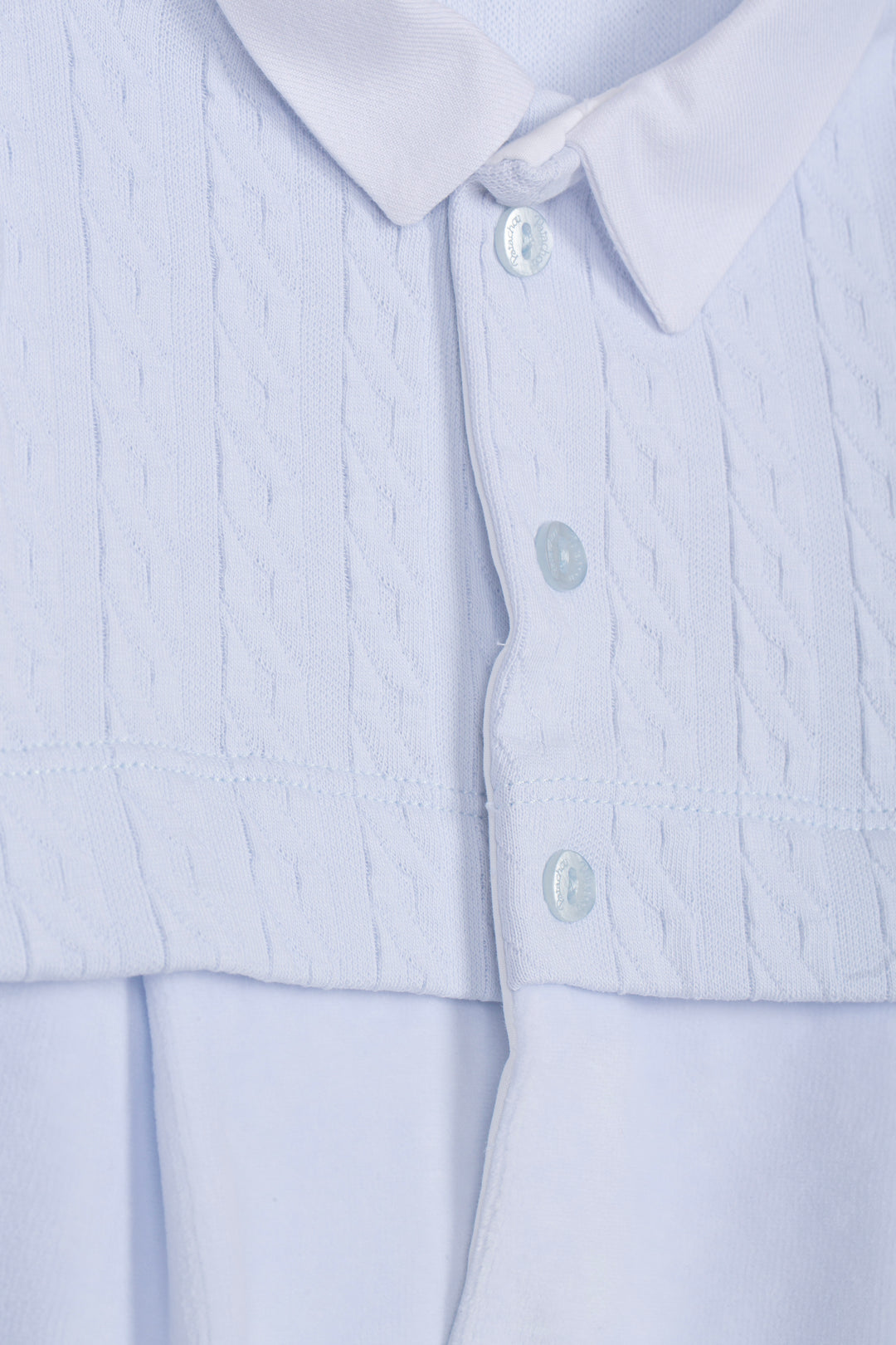 Close-up of a light blue collared shirt with a textured, vertically pleated front panel and smooth button-down lower section.
