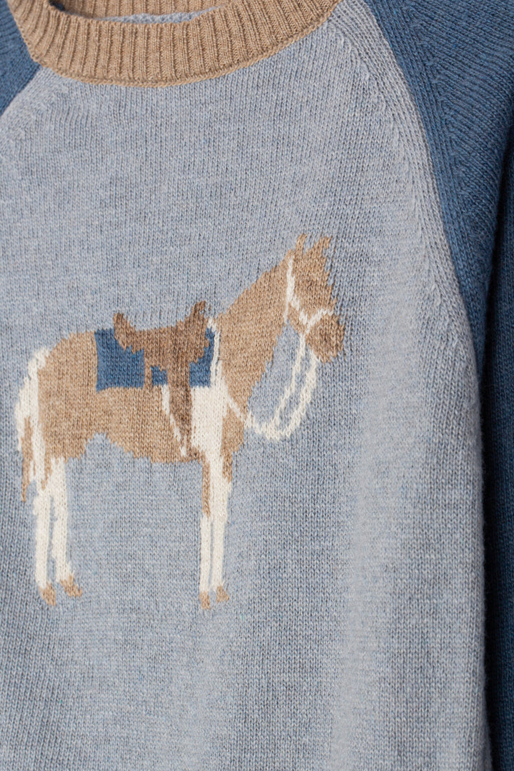 Close-up of a knit sweater with a horse motif in tan, cream, and blue on a light gray body, with a beige ribbed crew neck and blue raglan sleeves.