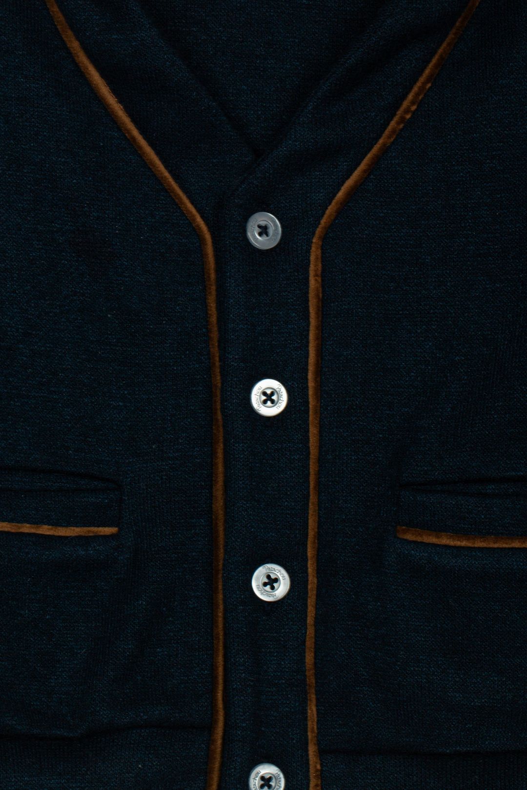 Close-up of a dark navy knit cardigan with brown contrast piping and silver buttons.