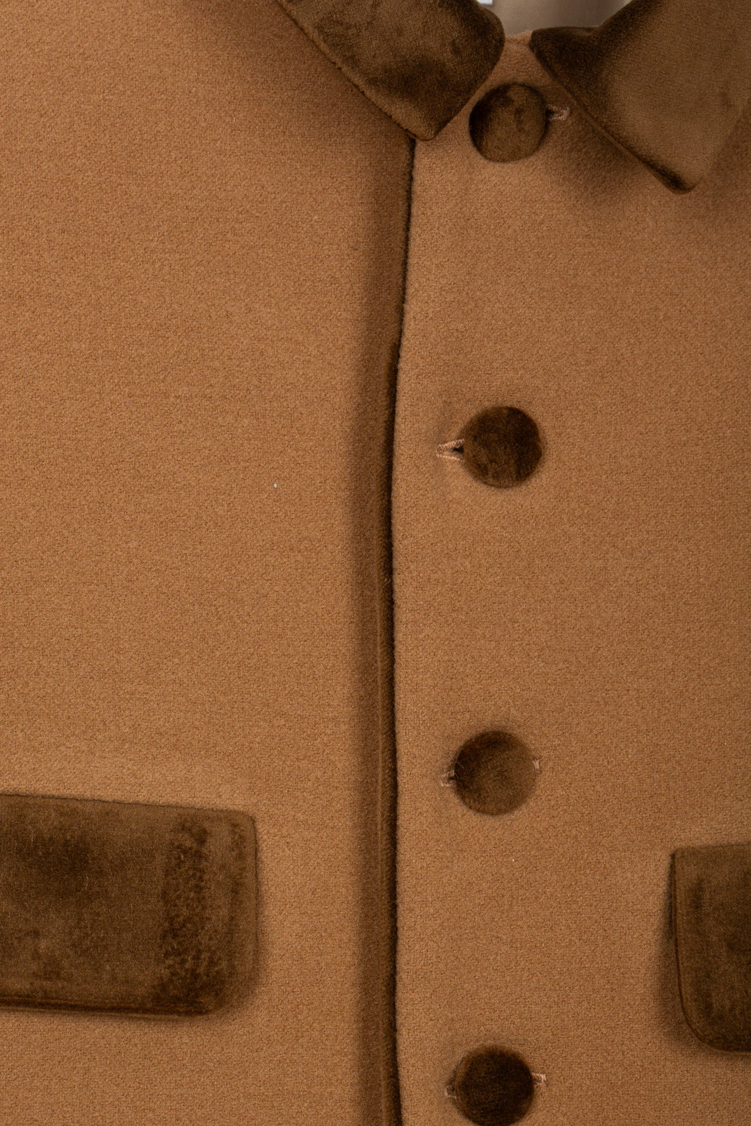 Close-up detail of a brown wool-like jacket or coat showing a button closure, collar, and pocket flaps.