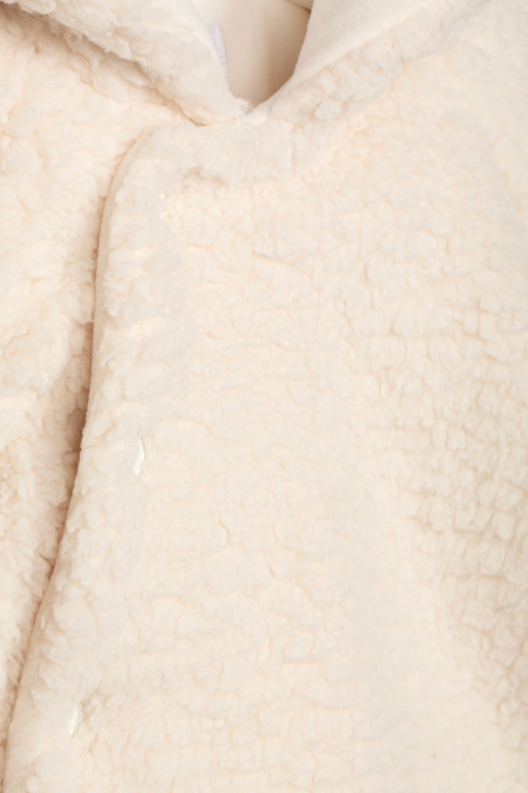 Close-up of a cream-colored sherpa fleece fabric, showing the soft, textured pile and a V-neck opening.