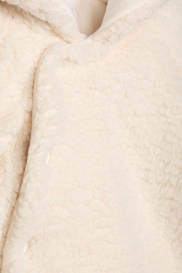Close-up of a cream-colored sherpa fleece fabric, showing the soft, textured pile and a V-neck opening.