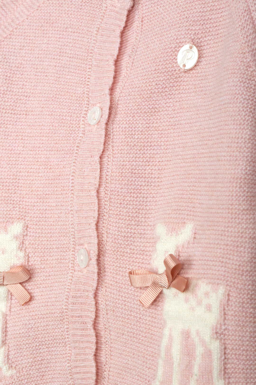 Close-up of a light pink knitted cardigan with white buttons, white embroidered deer motifs, and small pink ribbon bows.