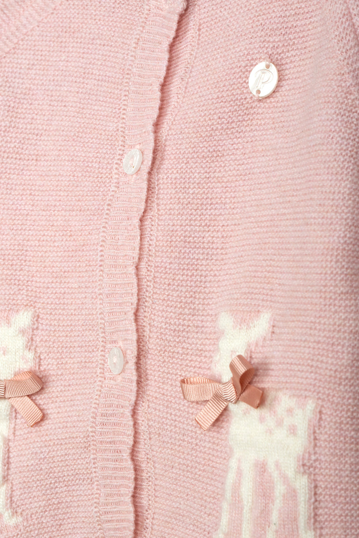 Close-up of a light pink knitted cardigan with white buttons, white embroidered deer motifs, and small pink ribbon bows.