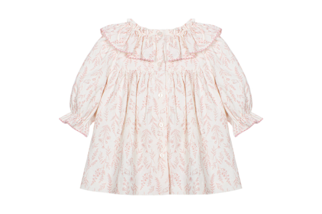 A baby girl's long-sleeve dress with a ruffled collar, featuring a delicate pink damask pattern on a warm cream background.
