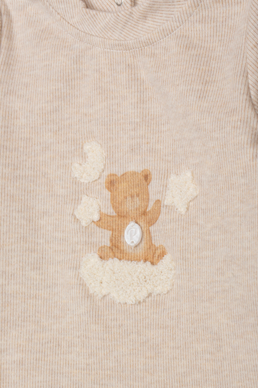 Close-up of a beige ribbed knit garment featuring a teddy bear applique sitting on a cloud motif on the chest.