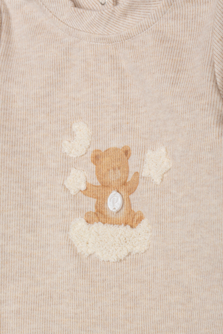 Close-up of a beige ribbed knit garment featuring a teddy bear applique sitting on a cloud motif on the chest.