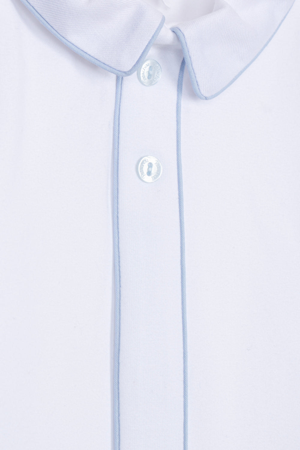 Close-up of a white collared shirt with light blue piping along the collar and placket, featuring white buttons.