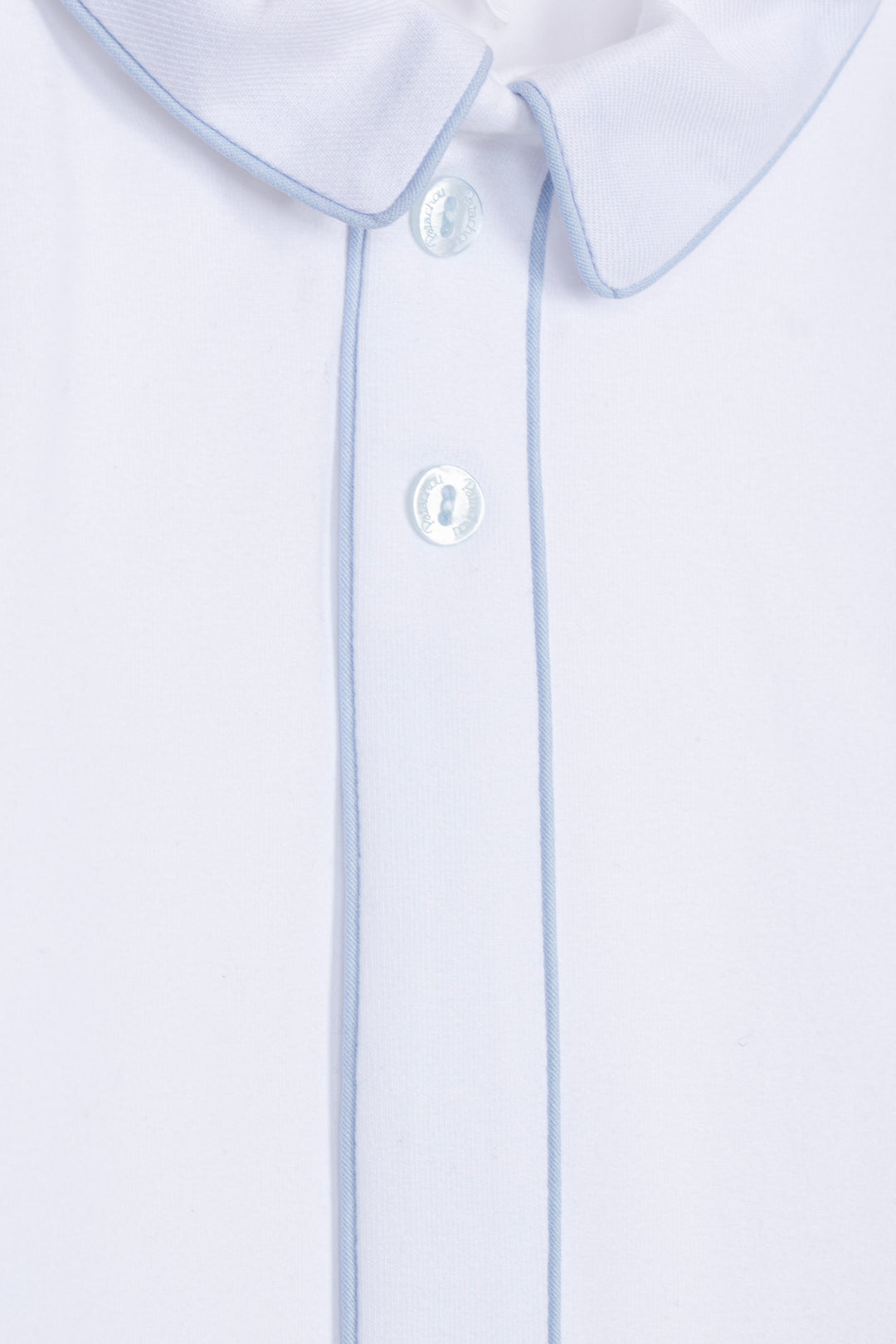 Close-up of a white collared shirt with light blue piping along the collar and placket, featuring white buttons.