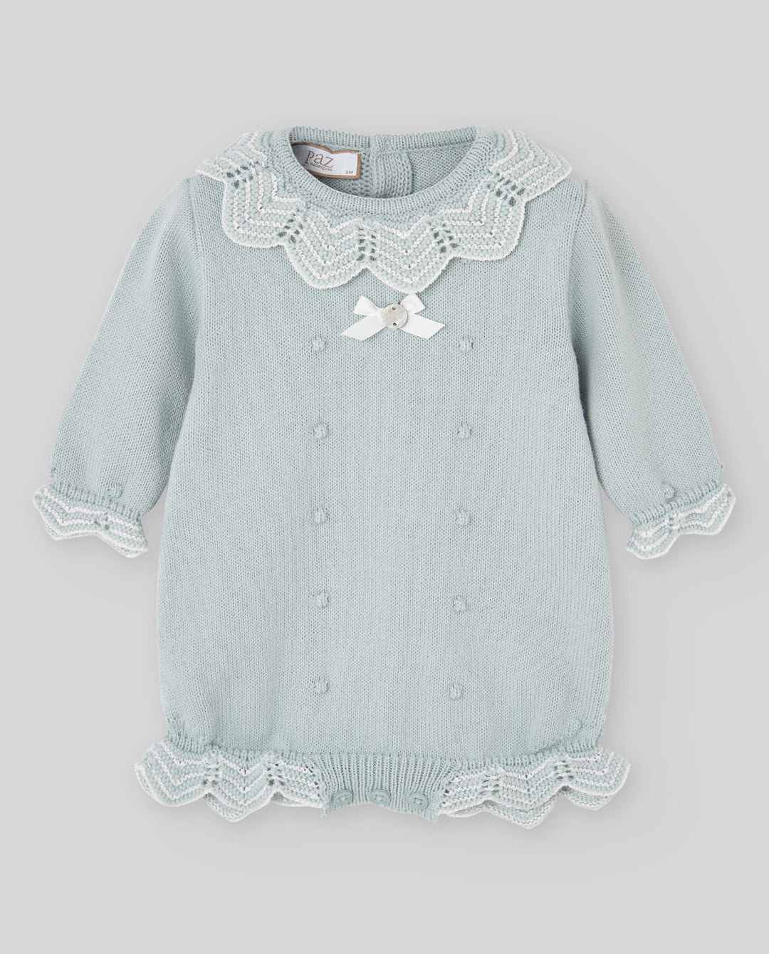 A light sage green baby knit romper with white lace collar, white lace cuffs, a white lace hem, and a small white bow at the chest.