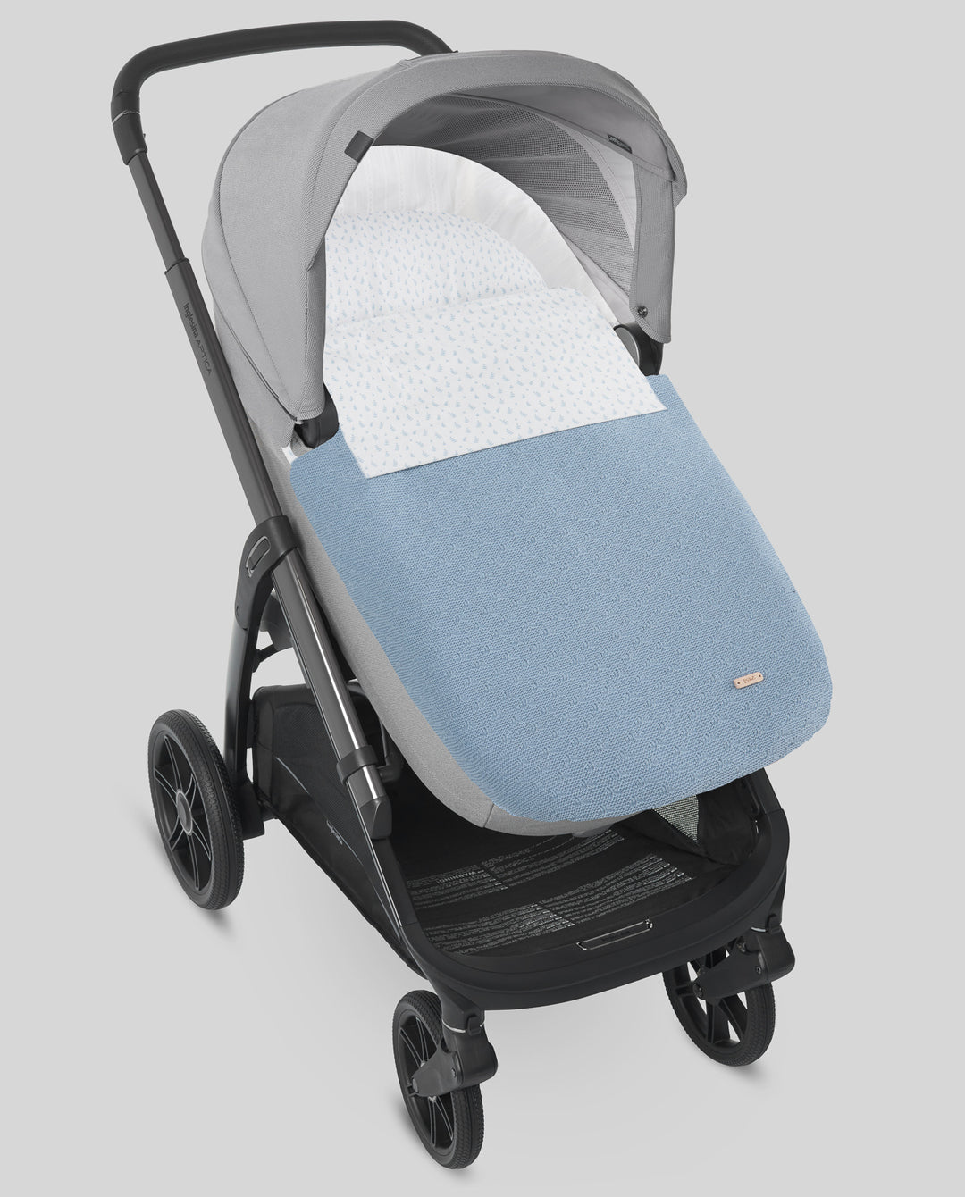 A stroller bassinet cover set in light blue and gray, shown fitted on a black stroller against a solid gray background.